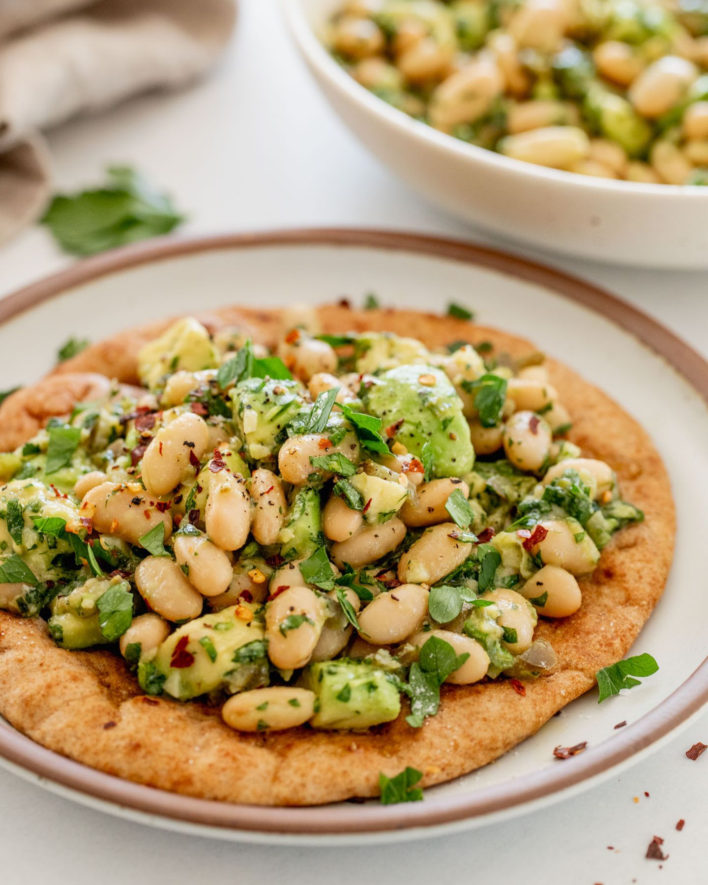 Flatbread topped with a mix of avocado and white beans with the bean mix featured in the background.
