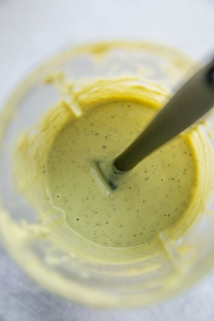 Stirring in dry dill into the avocado sauce in a blender cup.