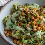 Side view of a baked shredded brussels sprout salad tossed together with roasted potatoes, chickpeas and avocado dressing.