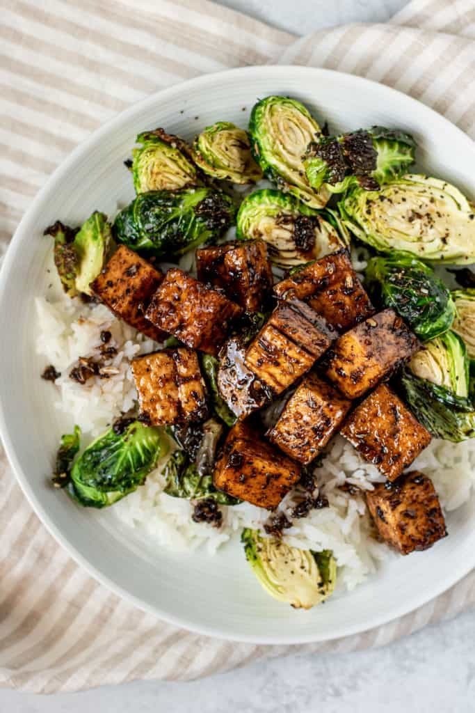 Close up of a plate of balsamic tofu on top of rice and brussel sprouts.
