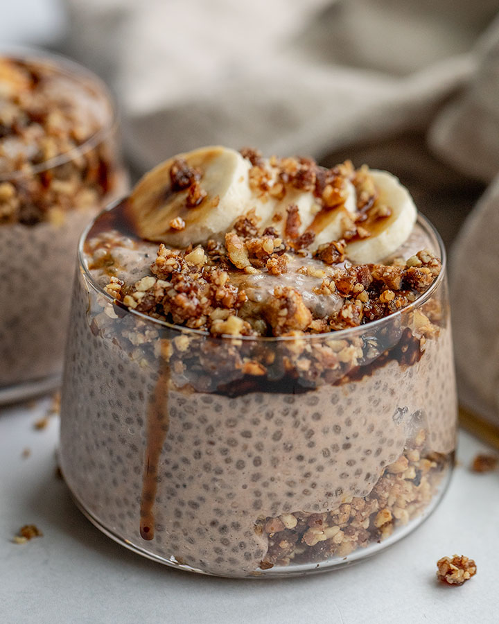 Close up of a jar of banana nut chia pudding layered with pecan crumble and date syrup.