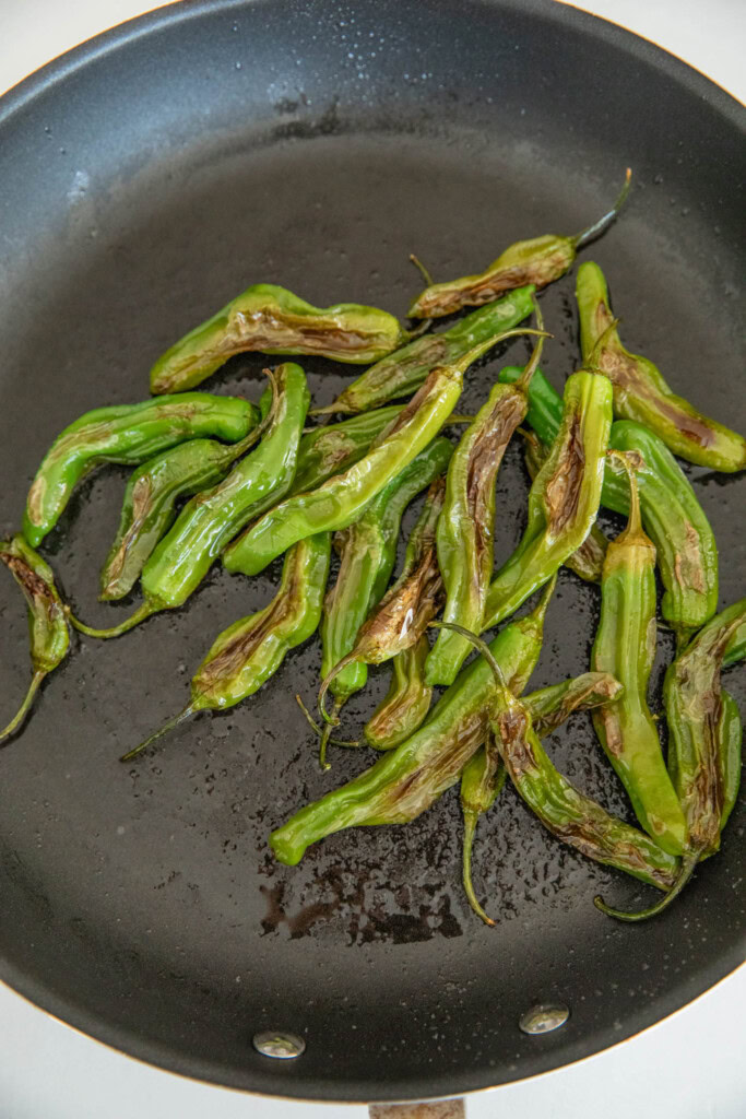 Blistered shishito peppers in a pan.