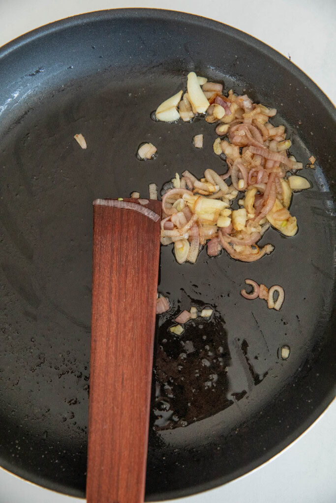 Sautéed shallots and garlic cloves in a pan.