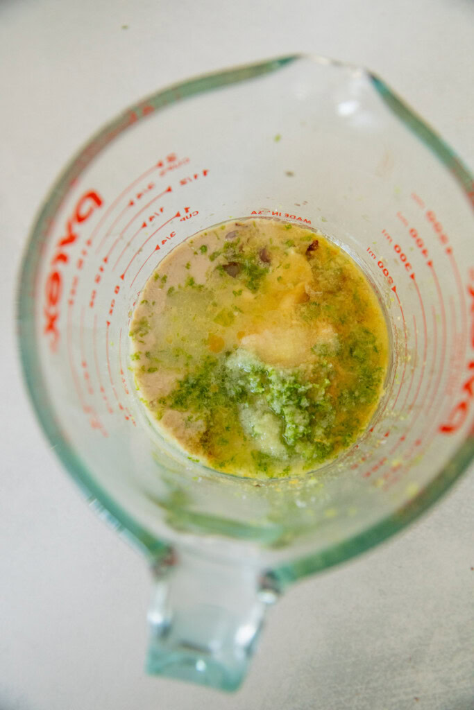 Large measuring cup with tahini, lime zest and juice, mustard, and nutritional yeast.