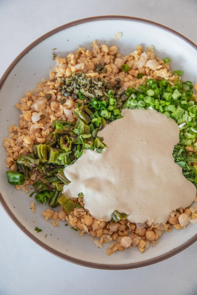 Mixing bowl filled with mashed chickpeas, capers, shishito peppers, scallions and the tahini sauce.