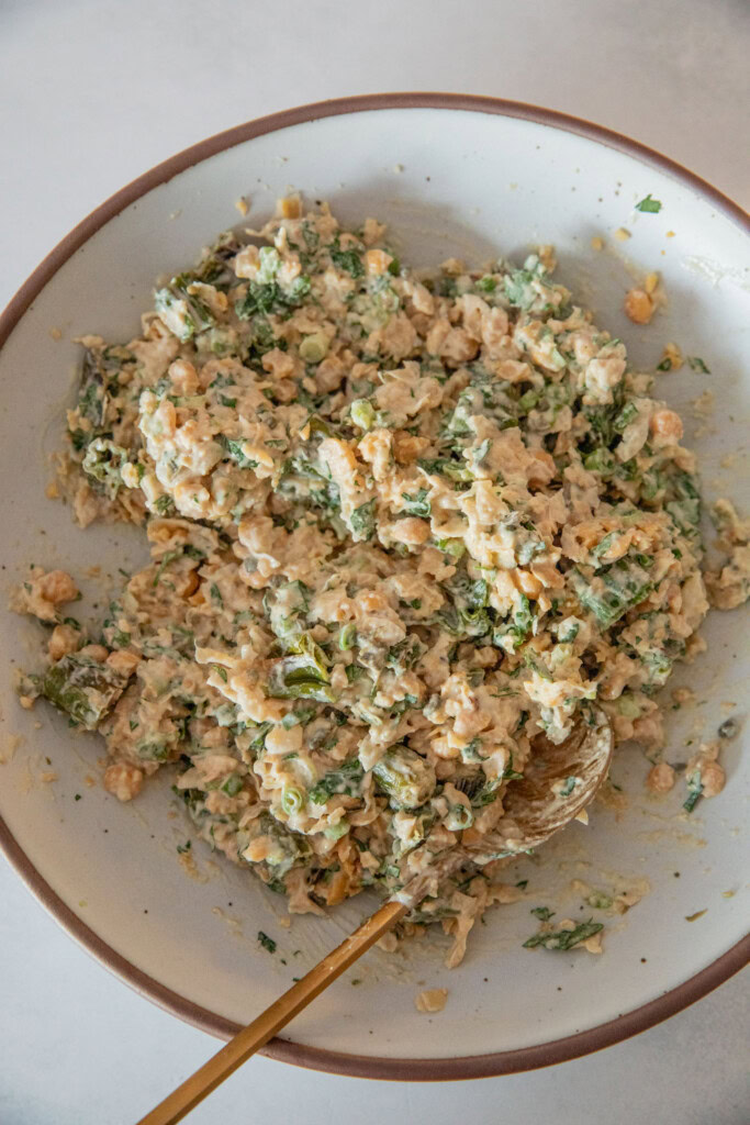 The chickpea mash with shishito peppers mixed together with the tahini dressing in a mixing bowl.