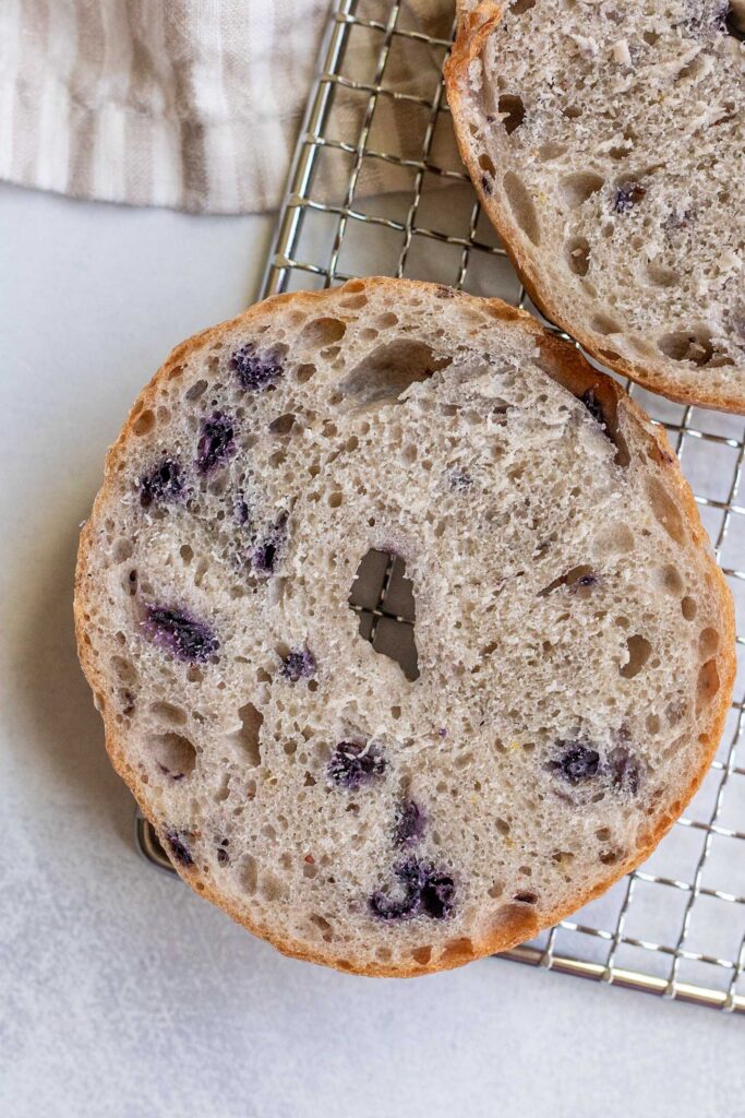 Blueberry bagel cut in half on a wire rack.