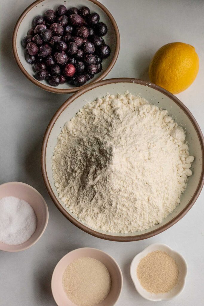 Bowl of thawed blueberries, flour, lemon, salt, sugar and yeast on a working surface.