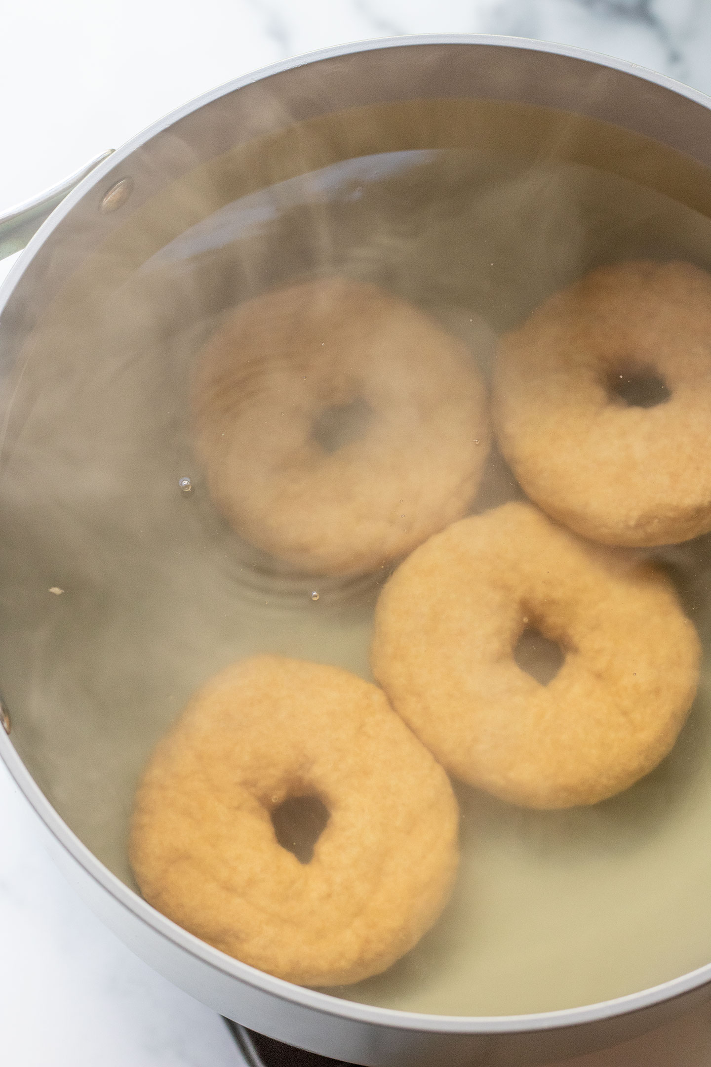 The uncooked bagel dough sinking to the bottom of the boiling water bath.