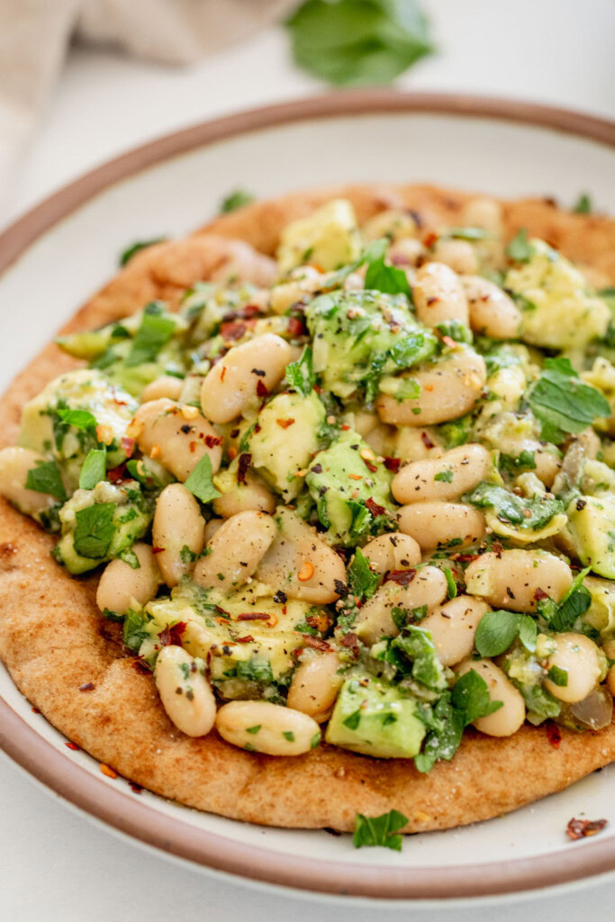 Close up of a plated flatbread topped with avocado white bean mix.
