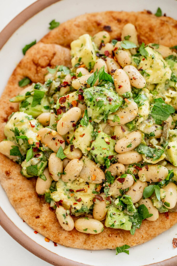 Top down close up of a flatbread topped with a mix of white beans and avocado chunks.