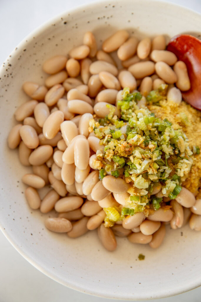 Bowl with white beans, nutritional yeast, cooked scallions and garlic.