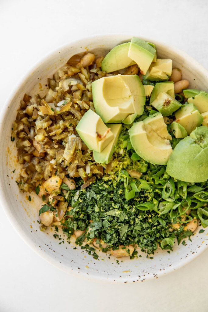 Bowl of white beans topped with pickled jalapeño, avocado and minced herbs and scallions.