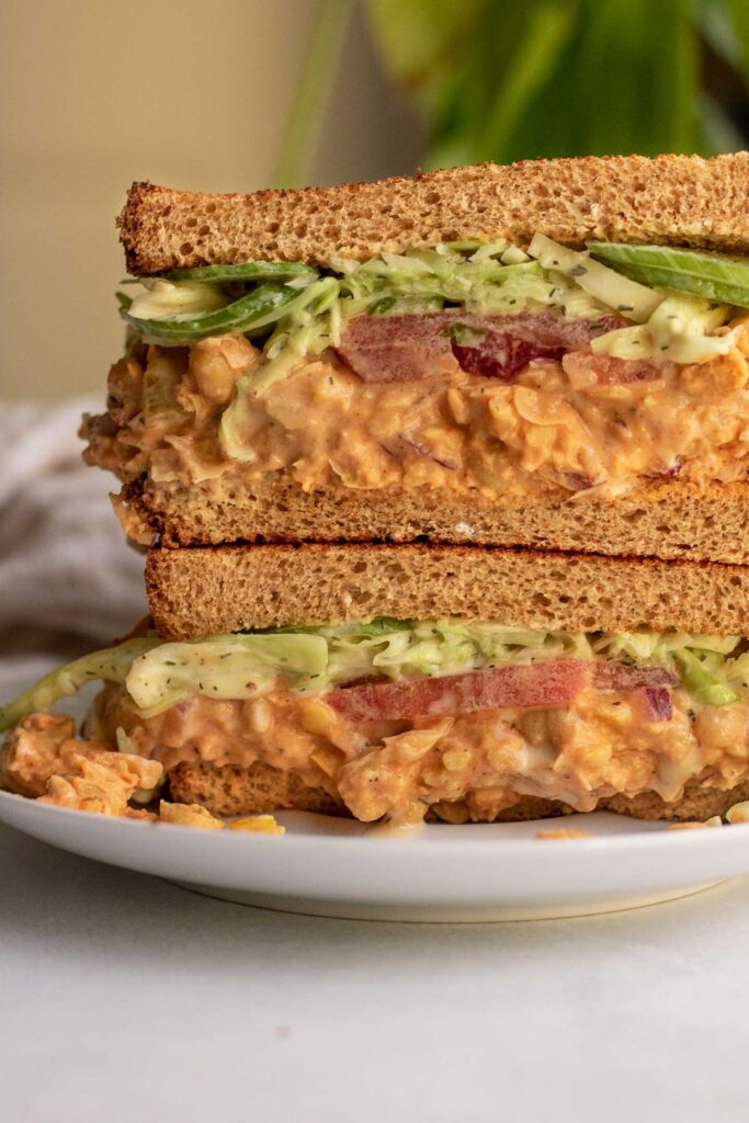 Buffalo chickpea salad sandwich topped with a tahini slaw stacked on a plate.