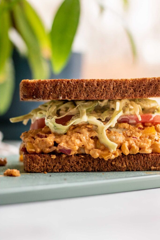 Fully assembled chickpea salad sandwich on a cutting board topped with tahini slaw.