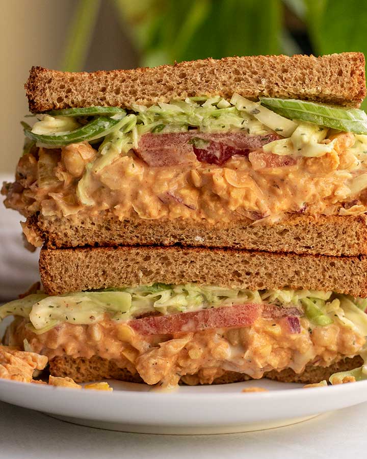 Chickpea salad sandwich stacked together on a plate filled with chickpea salad and tahini slaw.