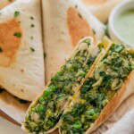 A potato leek wrap cut in half on a plate filled with toasted wraps behind it and a bowl of herby yogurt sauce.