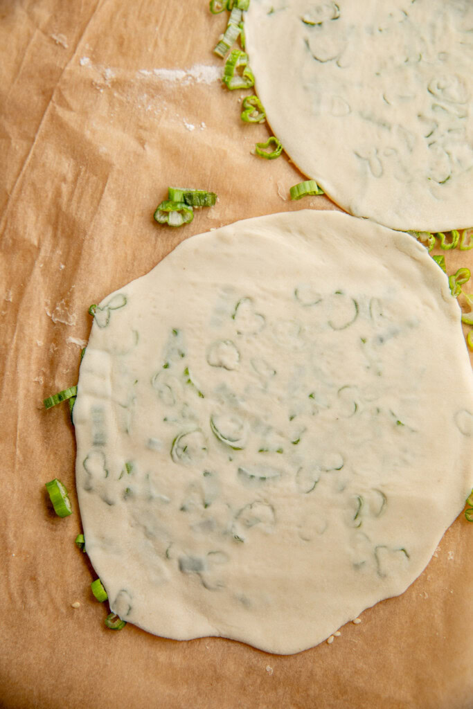 The scallion pancake rolled out thin on a flat surface.