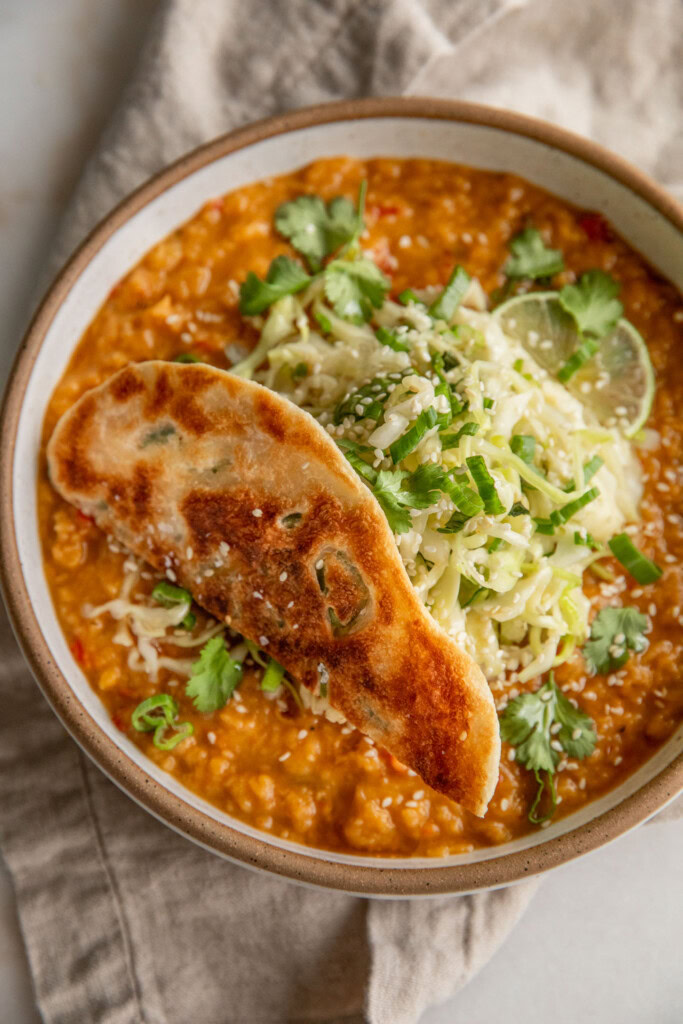 Bowl of cooked red lentils topped with cabbage slaw and a piece of scallion pancake on top.