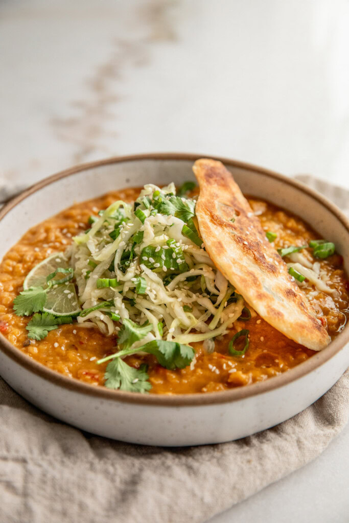Cooked red lentils in a bowl topped with cabbage slaw and a piece of a crispy scallion pancake.