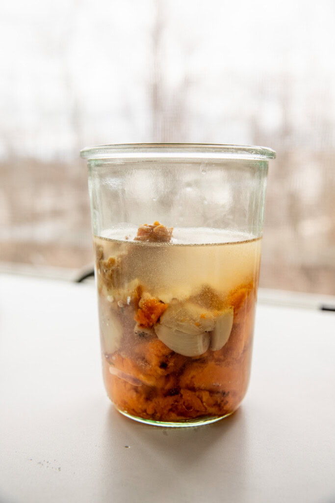 Blender cup with sweet potato, garlic, miso paste, and water ready to blend.