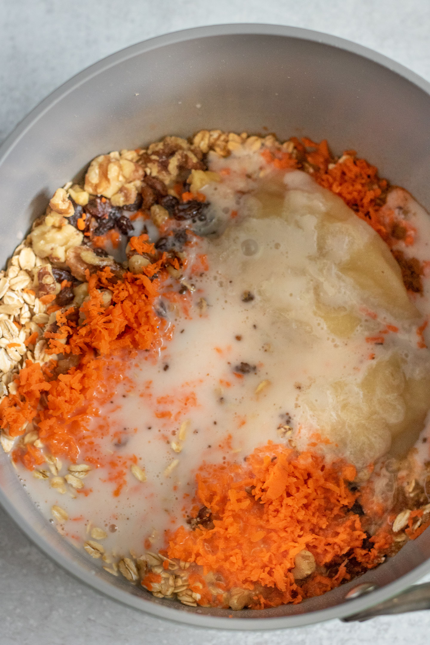 Sauce pan filled with oats, raisins, carrots, almond milk, spices, apple sauce, and shredded carrots.
