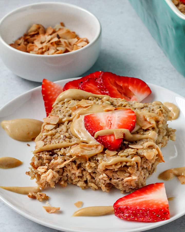 Baked oat square plated with strawberries and peanut sauce.