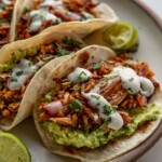 Side view of a plate of tacos filled with mashed avocado, shredded tofu topped with crema.
