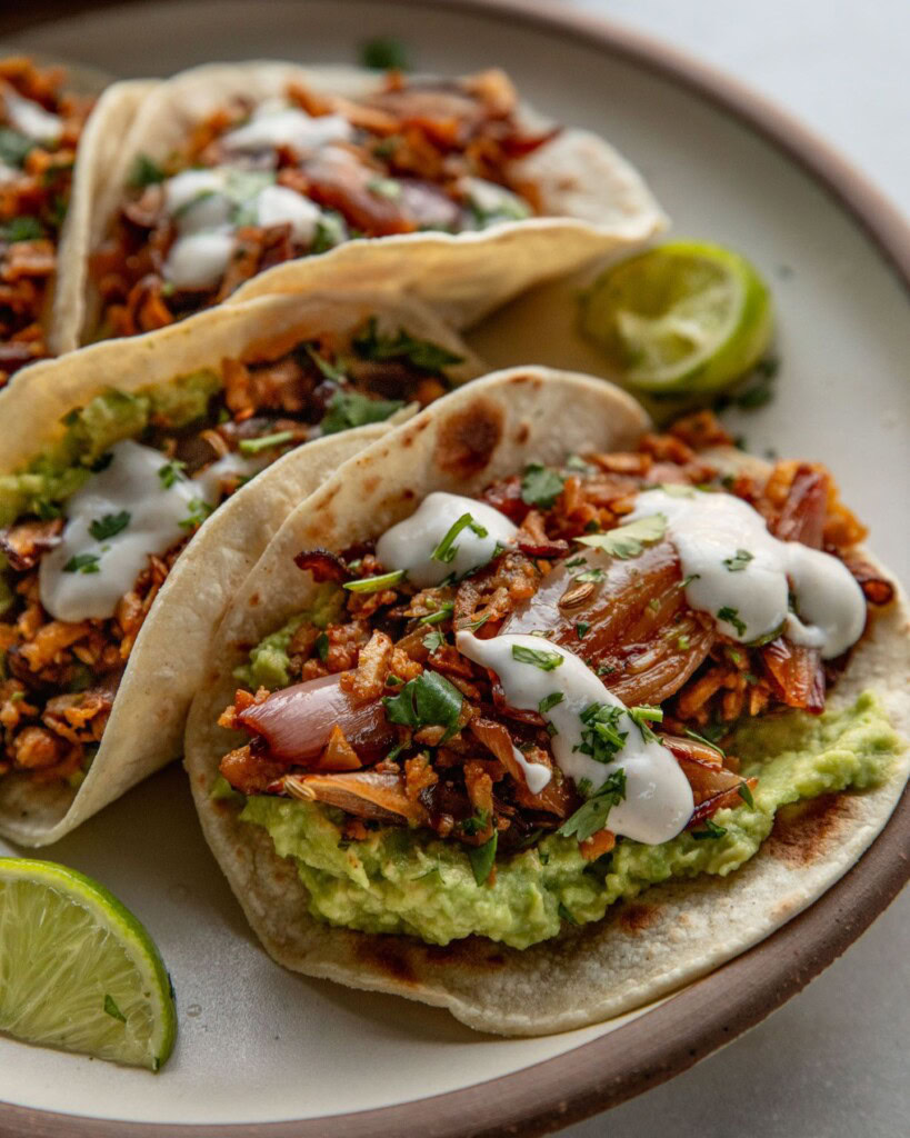 Side view of a plate of tacos filled with mashed avocado, shredded tofu topped with crema.