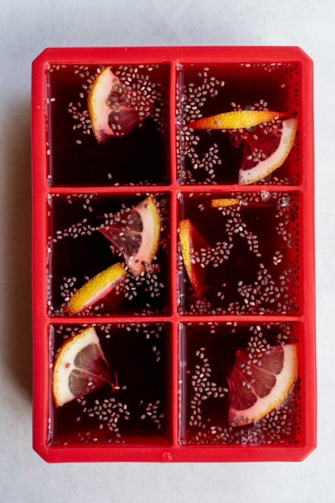 Combining the chia seeds, hibiscus tea, lemon slices, lemon juice and maple syrup in an ice cube tray.