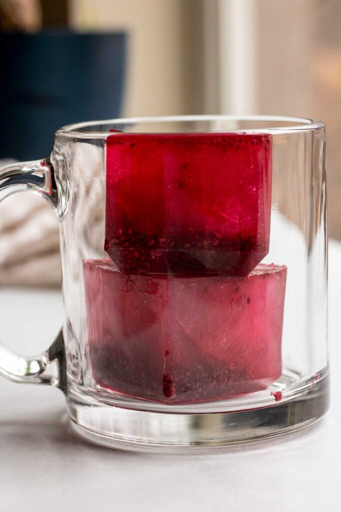 Two bright pink chia seed ice cubes in an empty glass mug.