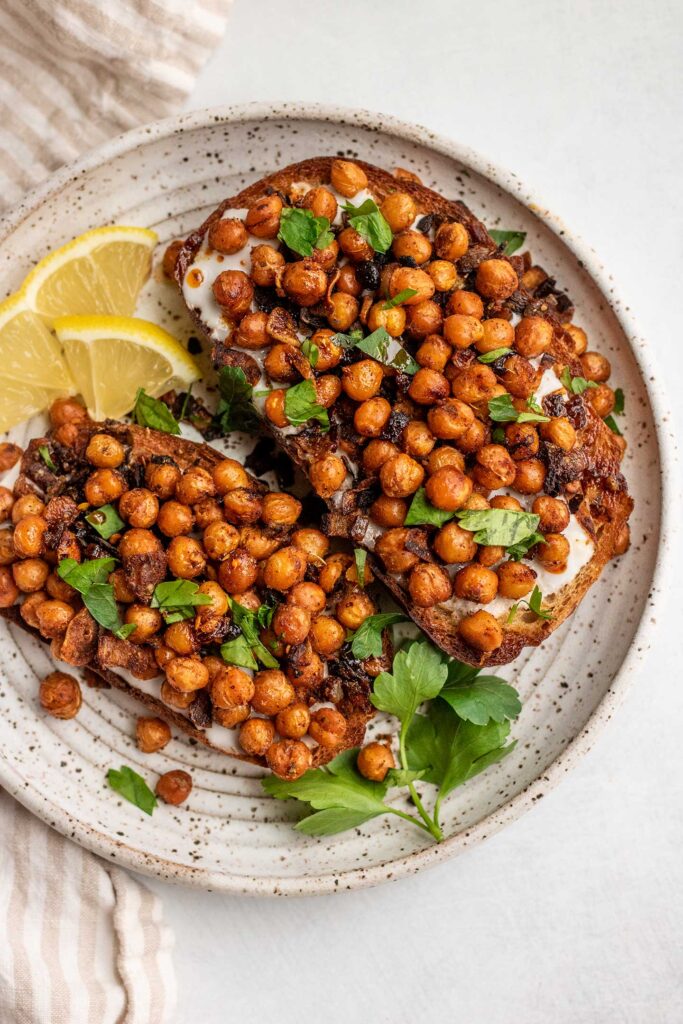 Breakfast toast served with chickpeas on top and served with lemon wedges.