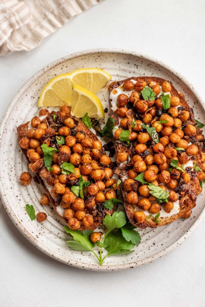 Top down view of a plate of chickpea breakfast toast served with extra lemon wedges and parsley.