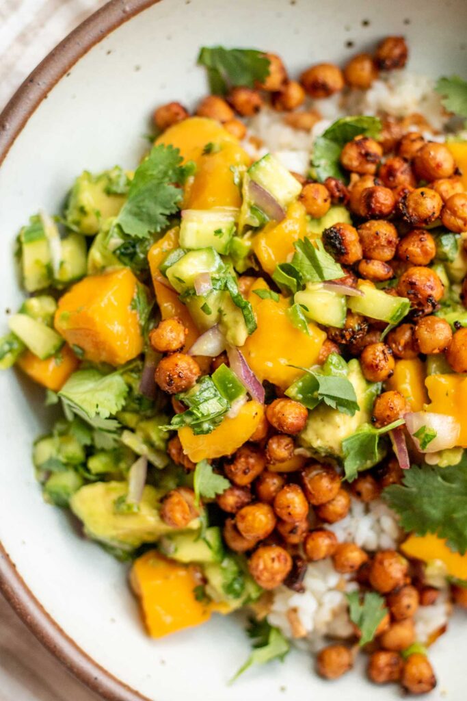 Close up view of a white bowl filled with tofu rice, mango salad and crispy chickpeas.