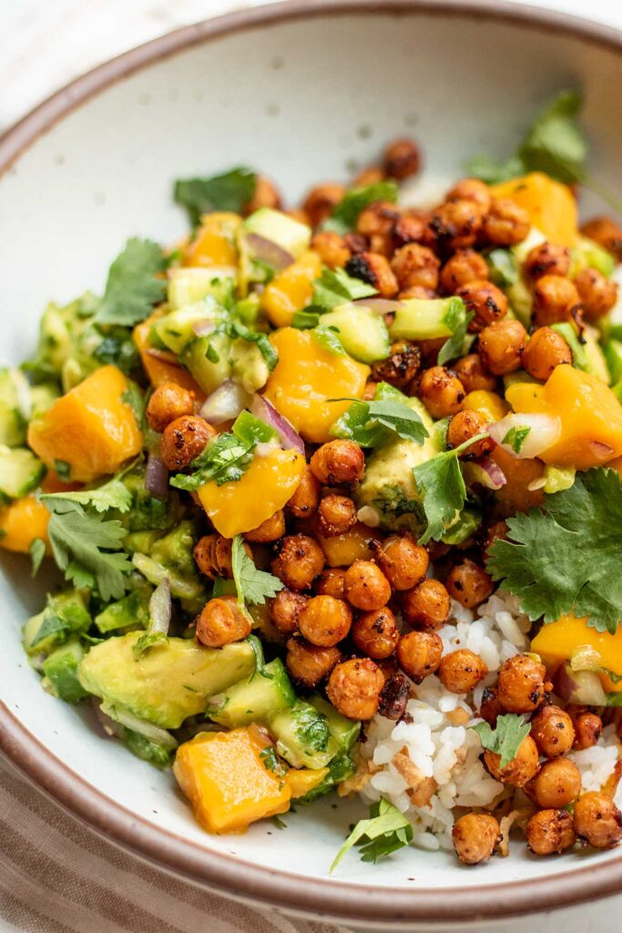 Side view of a white bowl filled with protein rice, crispy chickpeas and a serving of mango avocado salad.