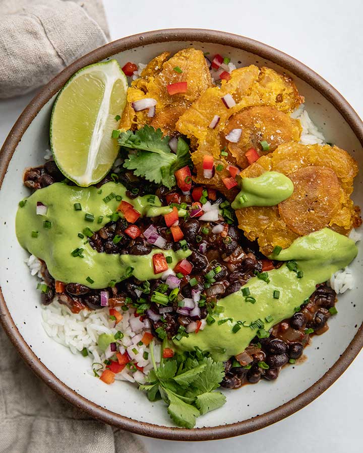 Bowl of rice topped with chipotle black beans and an avocado cilantro sauce with plantains arranged to the side.