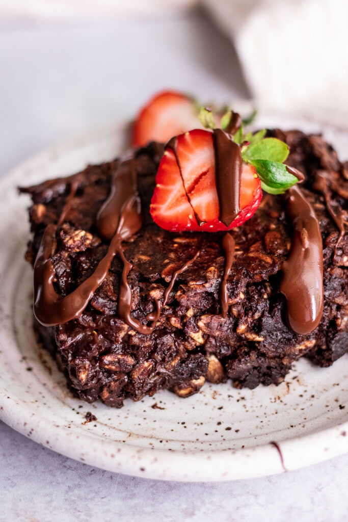 Side view of chocolate baked oatmeal topped with chocolate drizzle and strawberries on a plate.