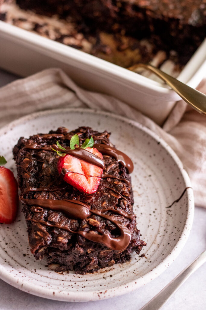 Plate of chocolate oats in front with a tray of baked oats in the background.