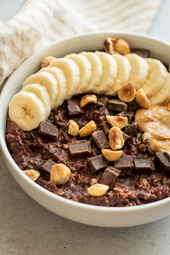 Side view of a bowl of oatmeal topped with banana, chocolate chips and roasted hazel nuts.