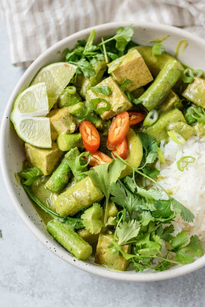 Angled side view of the coconut curry along with some rice and lime wedges.