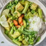 Bowl of coconut green curry served with rice and lime wedges.