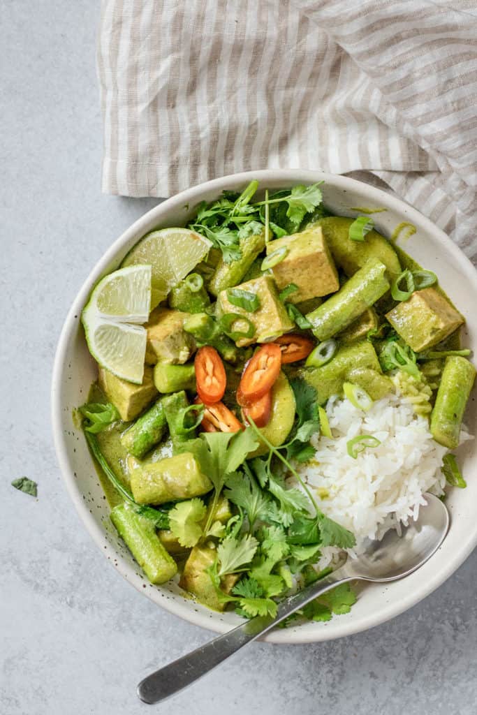 Bowl of curry topped with red peppers and scallions.