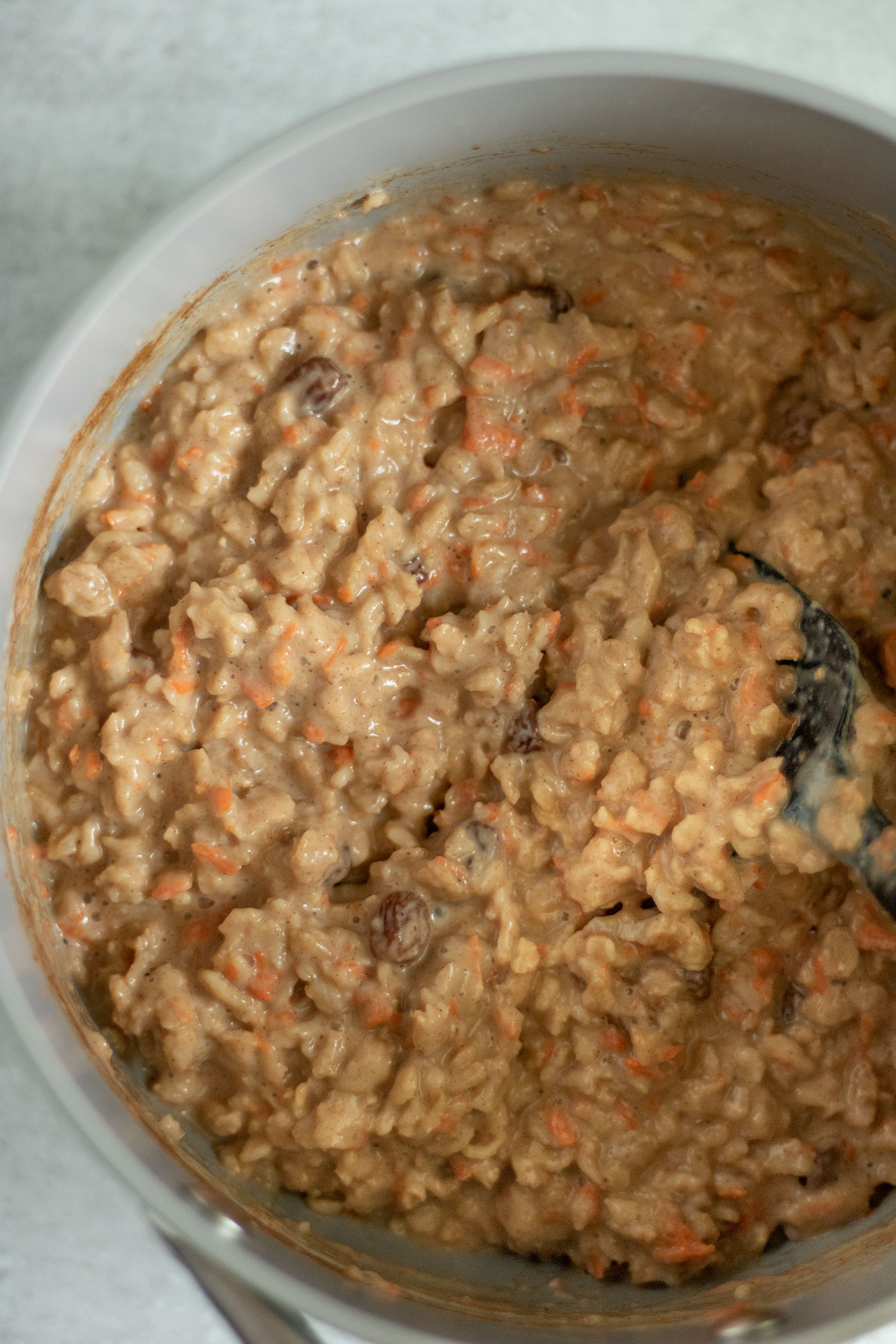 Cooked carrot cake oatmeal in a sauce pan being stirred with a spatula.