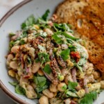 Close up of a bowl of bean salad with a piece of toasted bread in the background.
