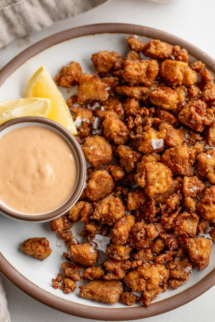 Plate of baked tofu nuggets served with a small bowl of yogurt sauce and lemon wedges on the side.