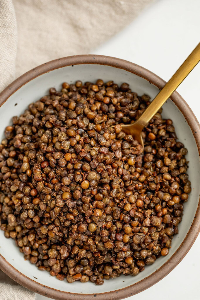 Close up of a bowl of lentils with a spoon tucked into it.
