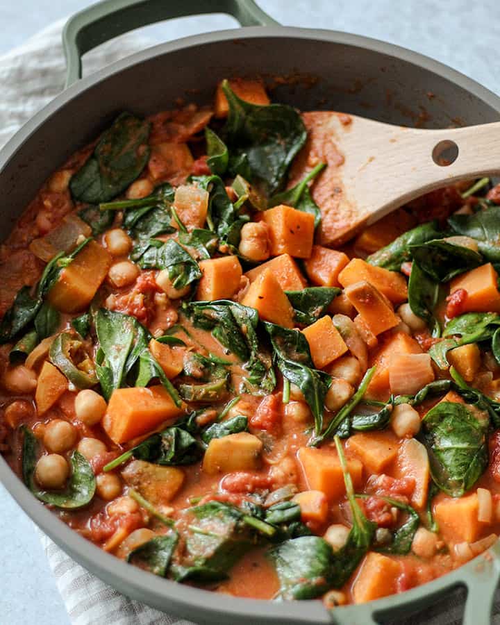 Tomato stew being stireed with a wooden spatula in a green trimmed pan.