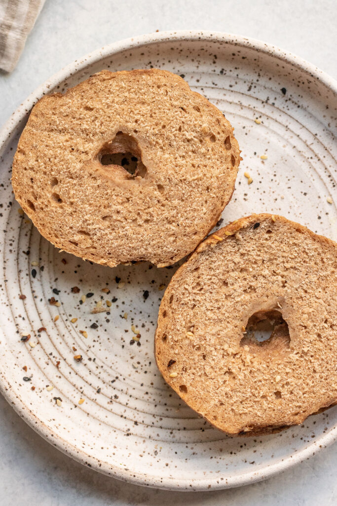 A bagel cut in half on a white plate.