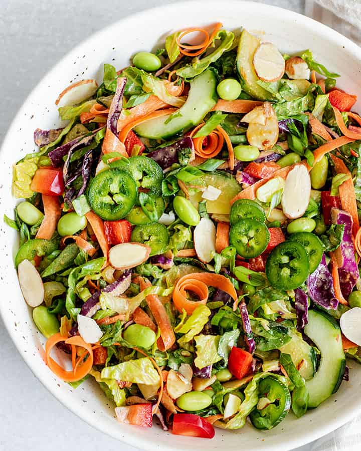 Bowl of edamame salad with a bunch of different vegetables and topped with dressing.