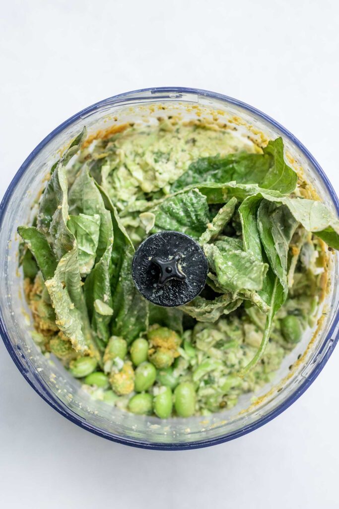Adding basil, edamame, nutritional yeast, lemon, garlic and tahini in a blender cup.